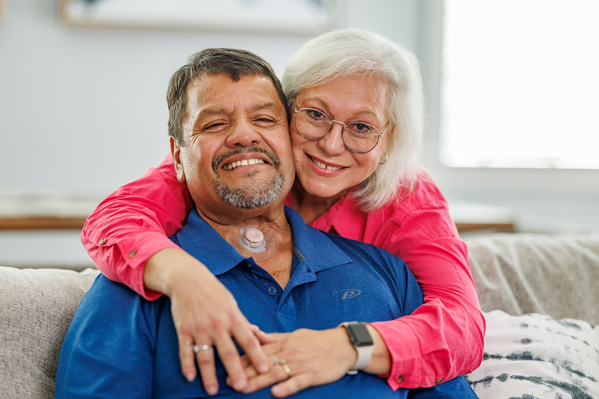 woman hugging man with a neck stoma sitting on couch